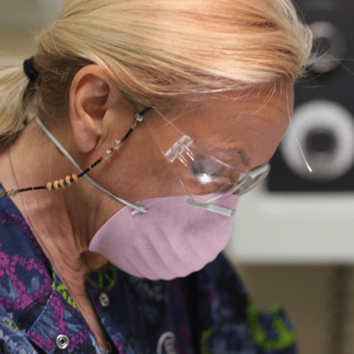 A close up of a hygienist performing a cleaning with protective mask and glasses on.