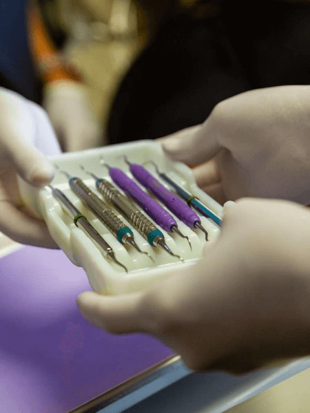 Close-up of dental tools in a tray being passed between two people in a dental office.