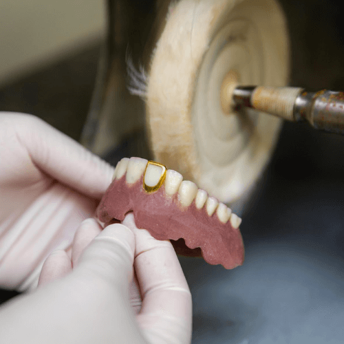 Close-up of a dental technician holding dentures while using a polishing wheel in a lab.